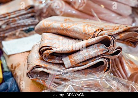 Gros plan d'un tissu décoratif ressemblant à de la soie avec des motifs tissés oranges et argentés détaillés. Banque D'Images