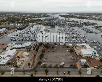 Vue aérienne d'une marina remplie de yachts et de bateaux reflétant la lumière, entourée de bâtiments et d'un parking, Mandurah, Australie occidentale, Aus Banque D'Images