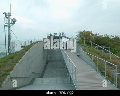 Terrasse d'observation en béton moderne avec passerelle en bois surélevée et garde-corps, visiteurs sur la plate-forme sur le toit, aménagement paysager à flanc de colline verte, antennes, overca Banque D'Images