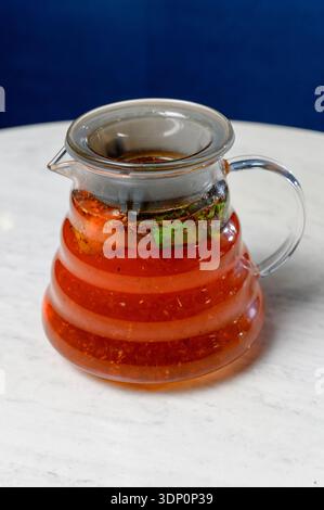 Tisane rouge avec feuilles de menthe et épices dans une théière transparente. Cafetière en verre avec thé épicé chaud et baies sur une table en marbre Banque D'Images