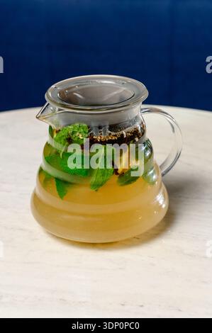 Théière en verre avec thé vert et feuilles de menthe fraîche. Une théière transparente avec tisane chaude et citron dans un intérieur de café Banque D'Images