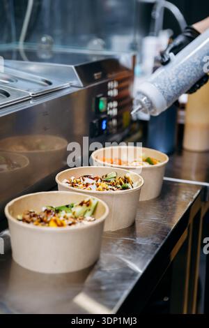 Sauce versée sur les saladiers à emporter sur le comptoir en acier inoxydable de la cuisine du restaurant Banque D'Images