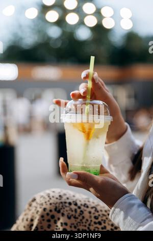 Femme tenant une boisson glacée au citron dans une tasse en plastique avec de la paille, café en plein air bokeh Banque D'Images