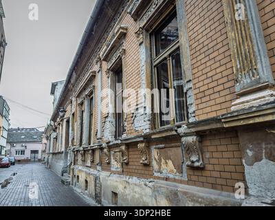 Façade de bâtiment historique en décomposition dans une rue de Pancevo, Serbie montrant du plâtre fissuré, des briques exposées et des ornements endommagés. Décadence urbaine et éco Banque D'Images