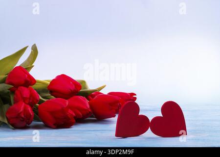 Tulipes rouges et deux coeurs en bois sur table bleue with copy space Banque D'Images