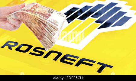 Samara, Russie - 27 mai 2023 : Rosneft Oil Company logo et pile de roubles russes dans la main. Rosneft est l'une des plus grandes compagnies pétrolières russes Banque D'Images