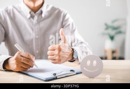 L'enquête de satisfaction reçoit un excellent avis des clients, remplit le formulaire de commentaires à la main, donne une note positive du service avec le pouce vers le haut, promeut Banque D'Images