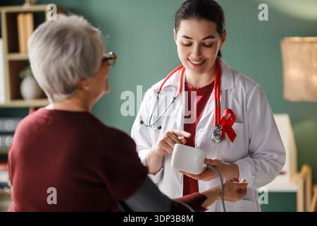 Professionnel de santé chaleureux et compatissant mesurant la pression artérielle d'une femme âgée dans un cabinet médical. Jeune docteur souriant en manteau blanc, portez Banque D'Images