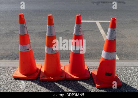 Quatre cônes de circulation orange avec bandes réfléchissantes alignées sur la chaussée. Banque D'Images