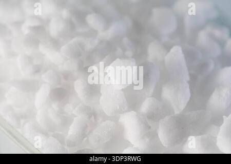 Vue macro d'une substance granulaire blanche brillante présentant des cristaux individuels aux surfaces inégales. Le matériau semble pur, utilisé pour le traitement de l'eau ou i Banque D'Images