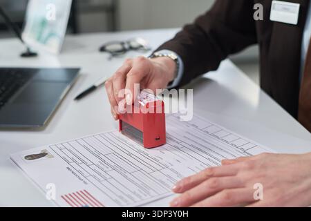 Femme traitant la demande de visa, main tenant le timbre approuvé rouge pressant le document avec la photo du demandeur visible, travaillant au bureau du centre des visas Banque D'Images