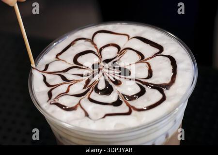 Barista qualifié créant une belle conception d'art de latte de fleur sur le dessus de la boisson de café. main utilise bâton pour dessiner avec de la sauce au chocolat sur délicieux mi crémeux Banque D'Images