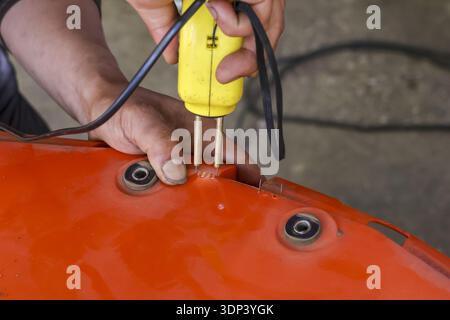 Un technicien concentré effectue la réparation sur le pare-chocs de voiture en plastique orange fissuré. À l'aide d'un pistolet de soudage à agrafes chaudes jaune pour l'entretien de carrosserie automobile dans Banque D'Images