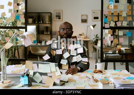 Portrait d'homme noir travaillant au bureau couvert de notes adhésives Banque D'Images