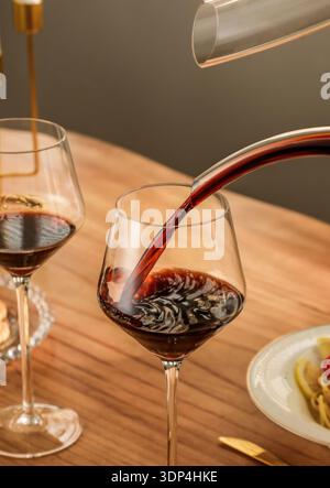 Verser le vin rouge de la carafe dans l'élégant verre de cristal sur la table en bois Banque D'Images