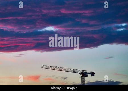 Silhouette de grue à tour contre les spectaculaires nuages violets de coucher de soleil sur le site de construction urbaine Banque D'Images