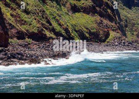 Côte atlantique rocheuse près de Porto Moniz Madère Portugal, les vagues se brisent sur les pierres volcaniques sous les falaises vertes et l'eau bleu clair révèle le surf le long Banque D'Images
