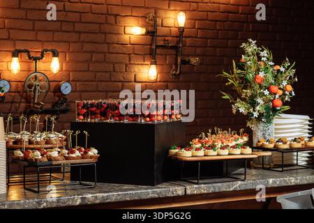 Table de restauration élégante avec verres à dose aux baies éclatantes, mini tartes assorties et canapés gastronomiques sur des surmontoirs noirs Banque D'Images