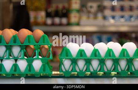 Oeufs frais assortis dans des plateaux en plastique vert réutilisables sur l'affichage, prêts à la vente dans un marché flou ou un fond de magasin. Alimentation saine. Source de Prote Banque D'Images