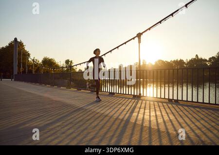 Jeune femme jogging sur le pont au bord de la rivière au lever du soleil, fitness en plein air dans le parc Banque D'Images
