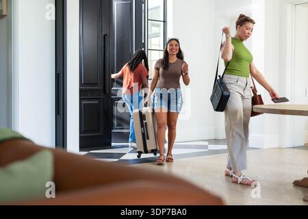 La femme du centre tire une valise à roulettes beige à travers les carreaux à carreaux dans l'entrée lumineuse près de la table Banque D'Images