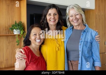 Diverses amies féminines avec femme senior posant dans le salon portant chemisier rouge, haut moutarde, TV Banque D'Images