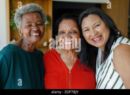 Amies afro-américaines souriantes, posant à la maison avec des étagères en bois, portant du rouge et du sarcelle Banque D'Images