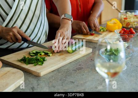 Les mains des cuisiniers tranchent le concombre, hachent les herbes et coupent les tomates sur des planches de bois avec du vin Banque D'Images