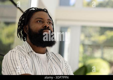 Homme afro-américain en chemise rayée debout avec les bras croisés, regardant vers le haut le mur de verre Banque D'Images