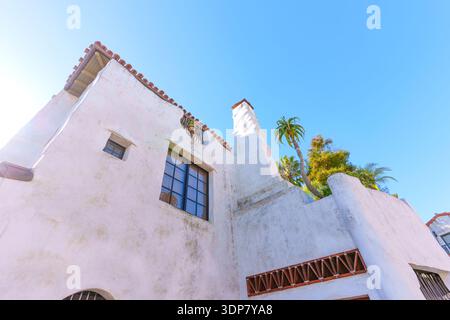 Vue vers le haut d'un bâtiment classique de Santa Barbara, avec stuc blanc, toit de tuiles rouges, et une cheminée, avec des palmiers et la lumière du soleil contre un c Banque D'Images