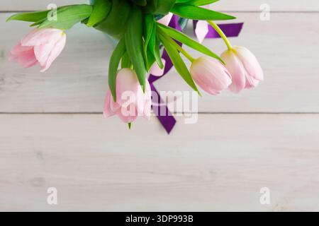Tulipes roses disposées avec des feuilles vertes et un ruban violet sur une table en bois Banque D'Images