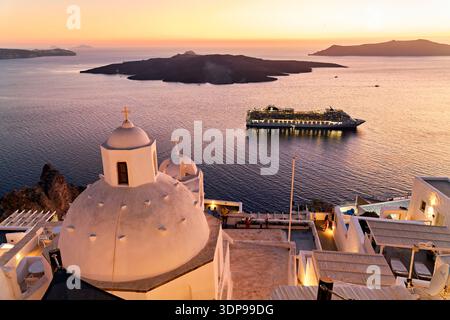 Un bateau de croisière ancre dans la caldeira de Santorin, en Grèce, tandis que les touristes apprécient la vue emblématique du coucher de soleil sur la mer Égée depuis les églises à dôme blanc et le cli Banque D'Images