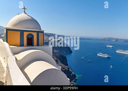 Église emblématique à dôme blanc à Santorin, en Grèce, surplombant la caldeira avec des bateaux de croisière et des bateaux. Les touristes visitent pour les vues imprenables. Banque D'Images