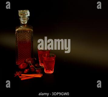 Liqueur de prunes de cerise à la cannelle et à l'anis dans une carafe en cristal et deux verres sur fond noir. Gros plan. Banque D'Images