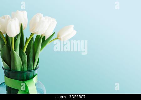 Tulipes blanches dans un vase vert placé sur un fond bleu clair dans un cadre simple Banque D'Images
