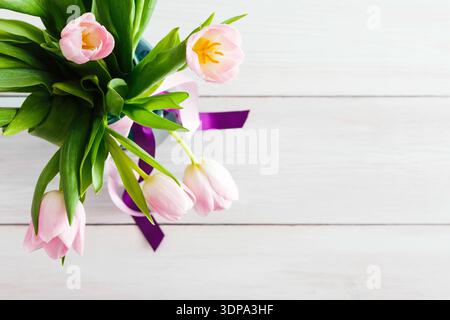 Tulipes roses dans un vase avec feuilles vertes et ruban violet sur surface en bois Banque D'Images