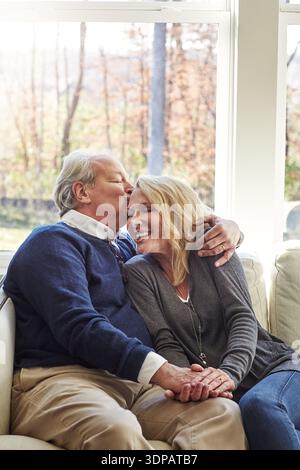 Rire, vieux couple et câlin sur le canapé, baiser et conversation drôle avec partenaire, liaison ou maison. Retraite, homme âgé et embrasser avec aîné Banque D'Images