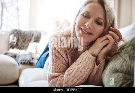 Souvenirs, se détendre et sourire de la femme sur le canapé dans le salon de la maison pour moi le temps de refroidissement ou de pause. Rupture, heureux et nostalgie avec la personne mature mentant Banque D'Images