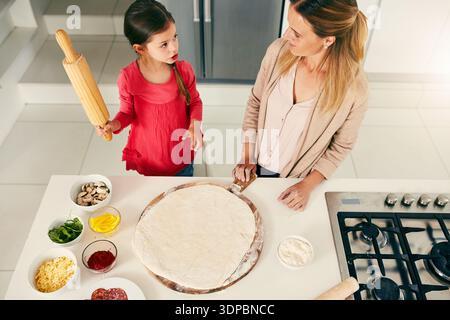 Cuisine, pizza et mère avec enfant dans la cuisine à la maison pour le repas, la nourriture ou le dîner ensemble. Angle élevé, rouleau à pâtisserie et maman avec fille pour préparer la pâte Banque D'Images