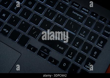 Une personne tape sur un clavier d'ordinateur portable dans une pièce sombre. Les touches sont allumées, montrant clairement la disposition. Il fait nuit dehors. Banque D'Images