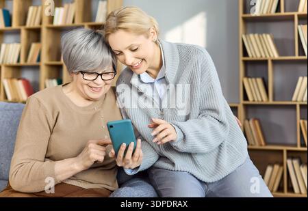 Happy Daughter montre les fonctionnalités du téléphone grand-mère pendant les appels vidéo à domicile chauds Banque D'Images