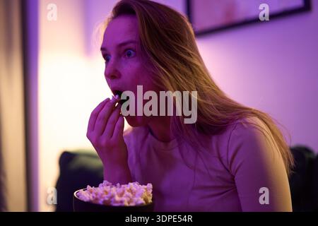 Femme adulte mangeant du pop-corn tout en regardant l'écran à la maison Banque D'Images