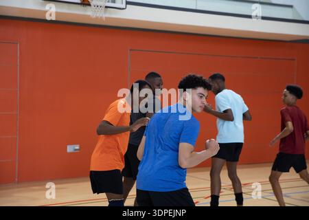 Adolescent masculin portant une chemise bleue, un short noir sprint sur un poing serrant sur un terrain de gymnastique, un câble d'écouteur Banque D'Images