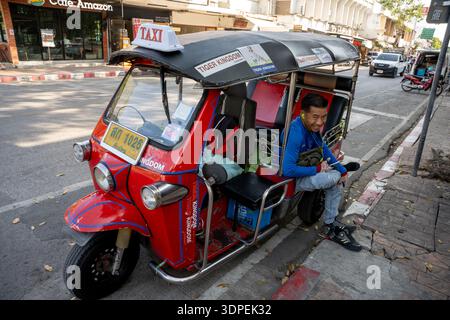 Un joyeux chauffeur de tuk-tuk thaïlandais sourit assis dans son taxi rouge emblématique, garé dans une rue ensoleillée de Chiang mai, en Thaïlande. Ce sho grand angle Banque D'Images