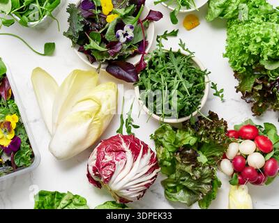 Des laitues fraîches et des légumes sont disposés sur un comptoir en marbre. Différents types de légumes verts sont prêts pour la préparation de salades. Les couleurs vives montrent la santé et Banque D'Images