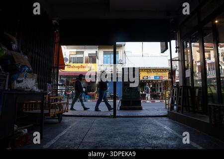 Photographie de rue à fort contraste prise depuis un point de vue sombre et couvert, encadrant une rue ensoleillée à Chiang mai, en Thaïlande. Des piétons silhouettes marchent Banque D'Images
