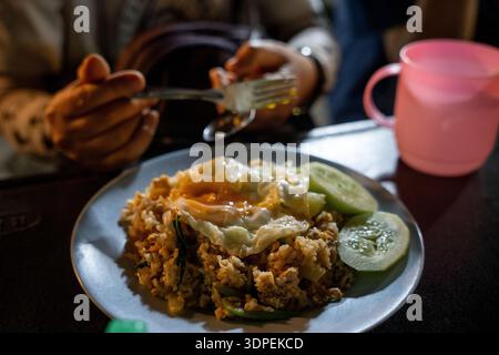 Une délicieuse assiette de riz frit indonésien (Nasi Goreng), un plat asiatique traditionnel, est servie avec un œuf frit ensoleillé et du concombre frais. En th Banque D'Images