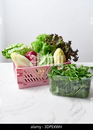 Différents types de laitues sont disposés dans des récipients sur un comptoir en marbre dans une cuisine. L'arrière-plan blanc et net améliore la disp des produits frais Banque D'Images