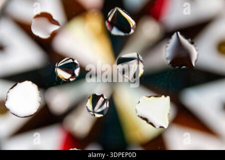 La photographie présente un motif géométrique vif en arrière-plan contrasté avec des gouttes d'eau scintillantes au premier plan, créant un lumineux et e Banque D'Images