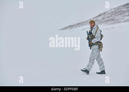 Soldat en camouflage d'hiver blanc marchant à travers le paysage de montagne enneigée avec fusil et équipement Banque D'Images